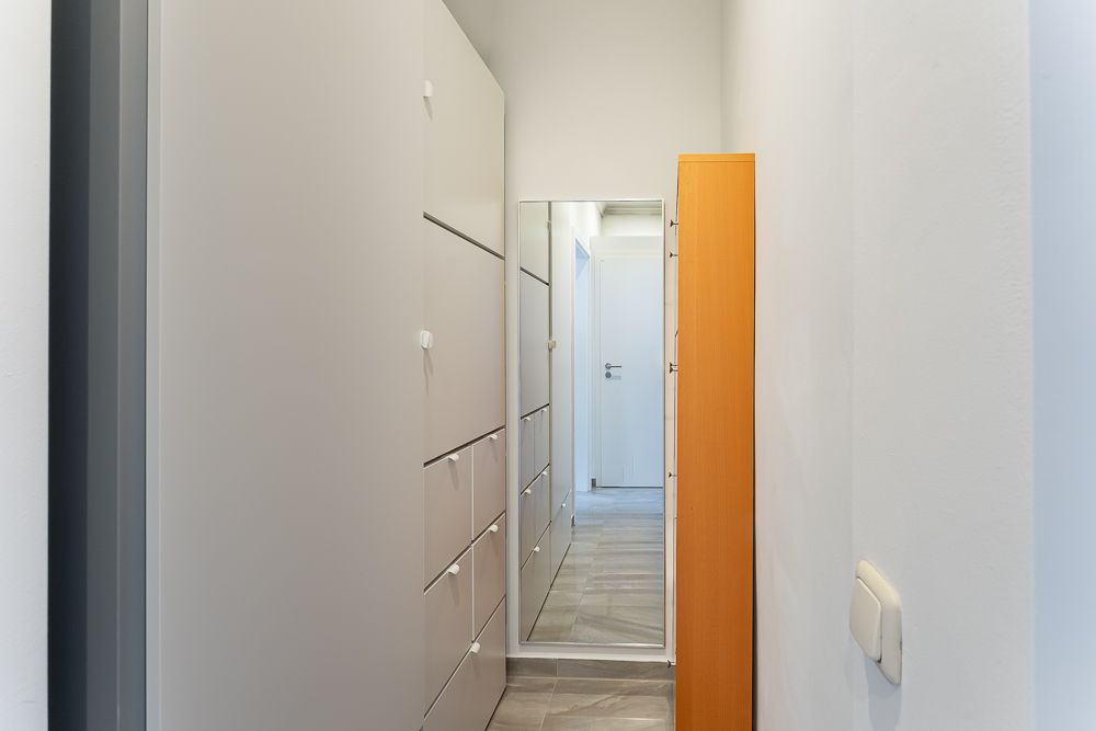 Schmaler Flur mit weißen Schränken, großem Spiegel und Holzmöbel an der Wand.