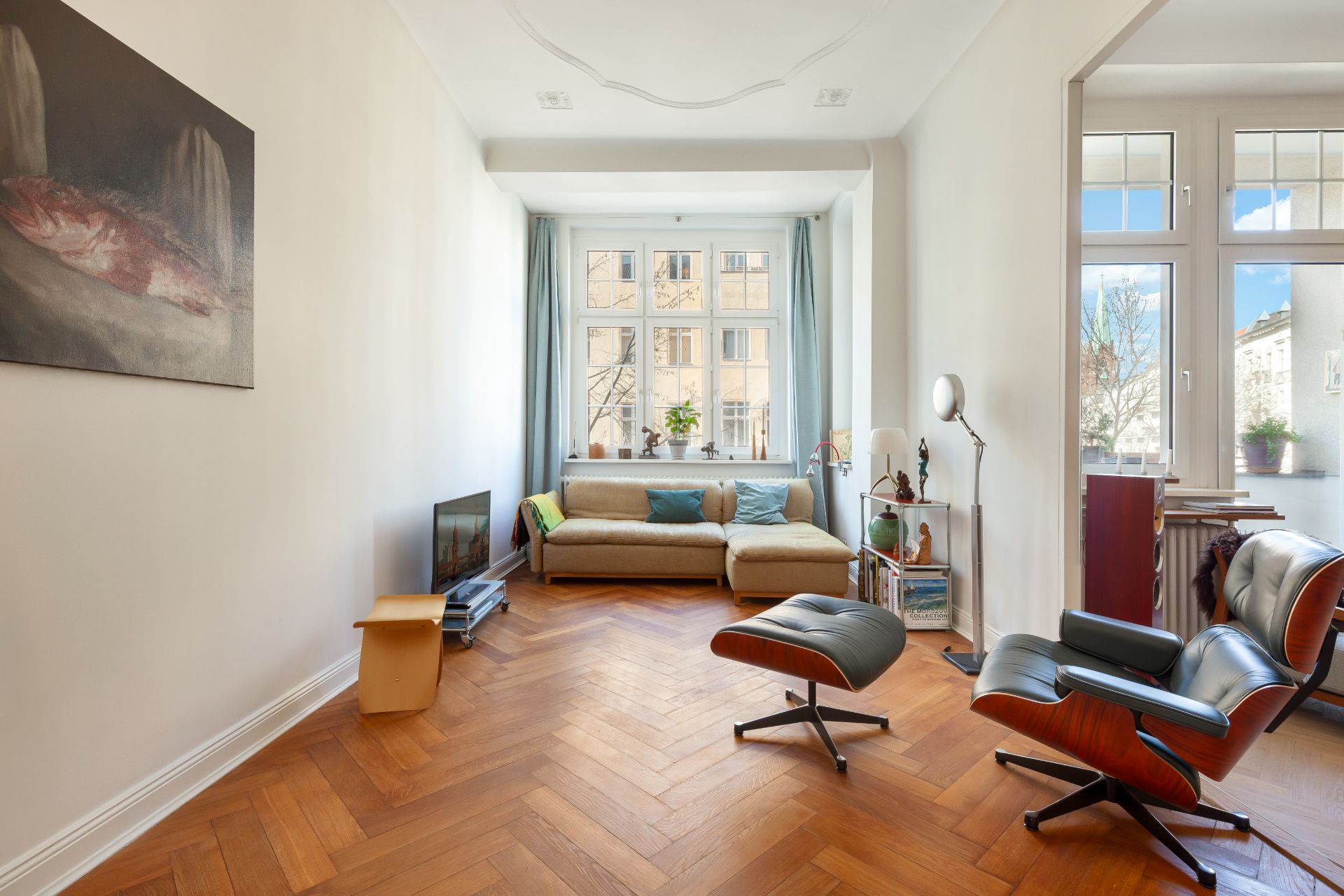 Helles Wohnzimmer mit Parkettboden, Sofa, Sessel, Couchtisch und großen Fenstern.