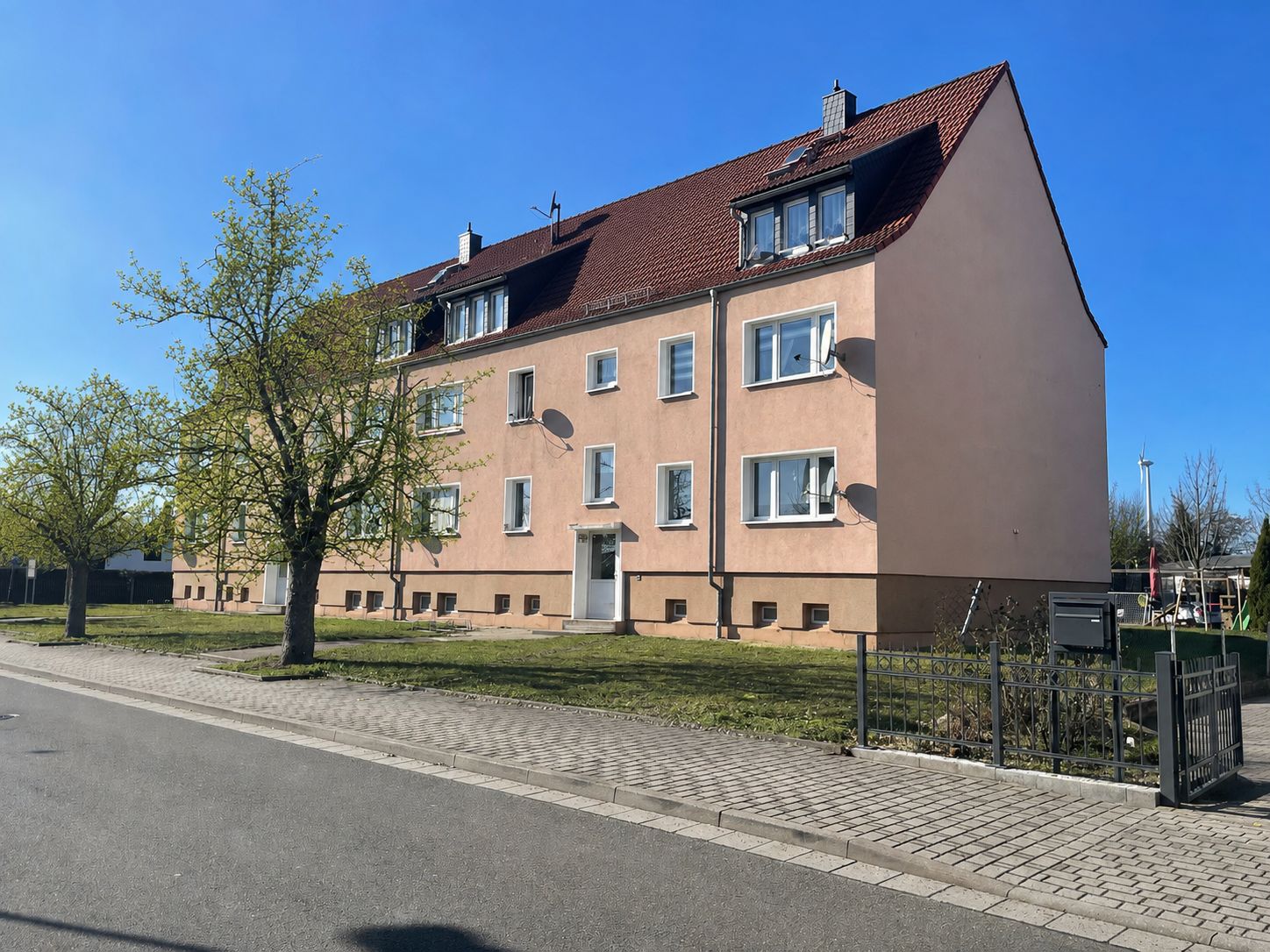 Dreistöckiges Wohnhaus mit roten Dachziegeln und Vorgarten an einer ruhigen Straße.