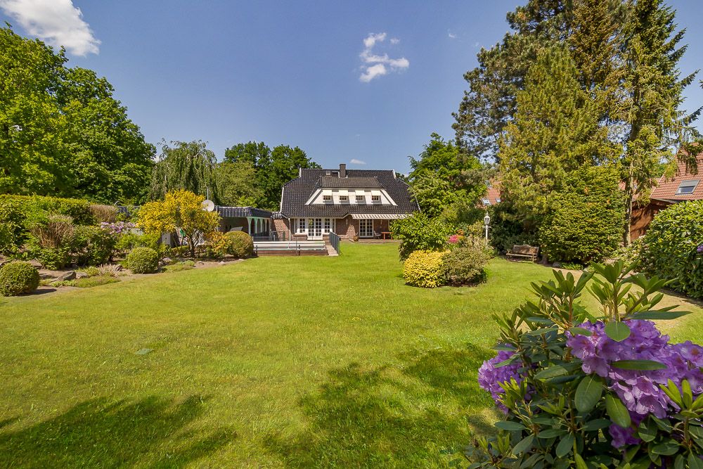 Haus mit dunklem Dach und großem, gepflegtem Garten mit vielen Bäumen und Blumen.
