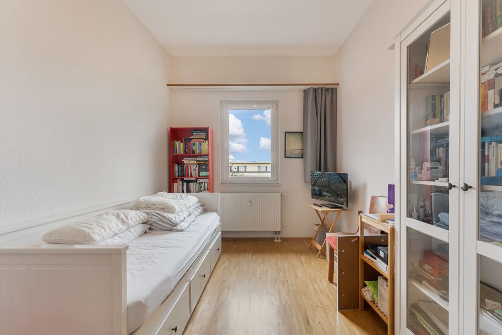Helles Zimmer mit Einzelbett, Bücherregalen, Fenster und Schrank auf Holzfußboden.