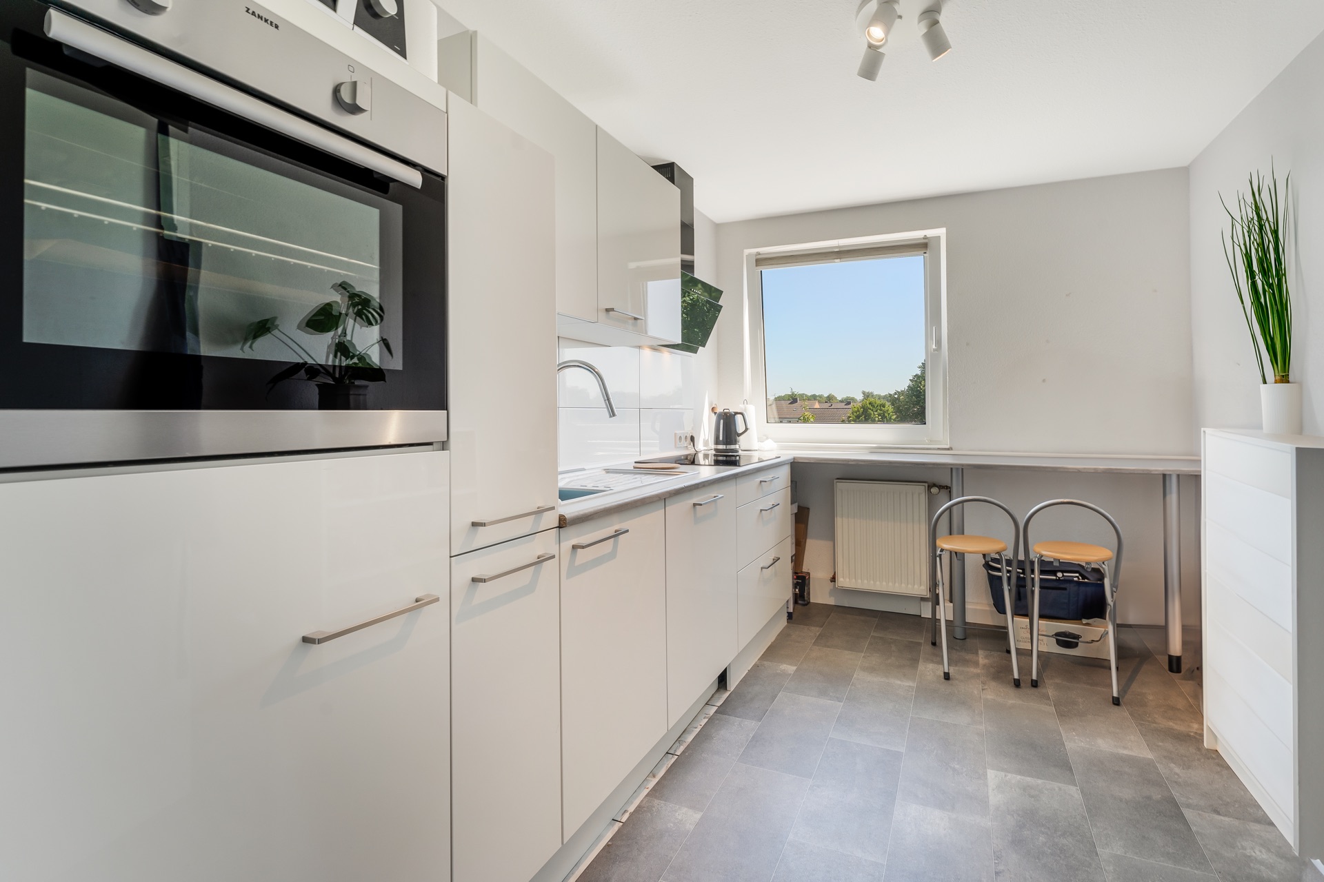 Moderne helle Küche mit Einbaugeräten, Fenster, Tisch und zwei Stühlen.