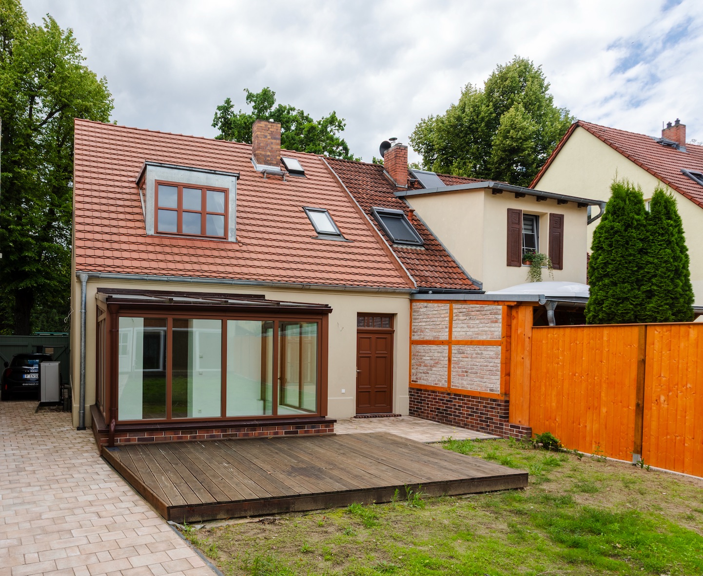 Rückansicht eines Hauses mit Wintergarten, Holzterrasse und Garten, daneben ein Holzzaun.