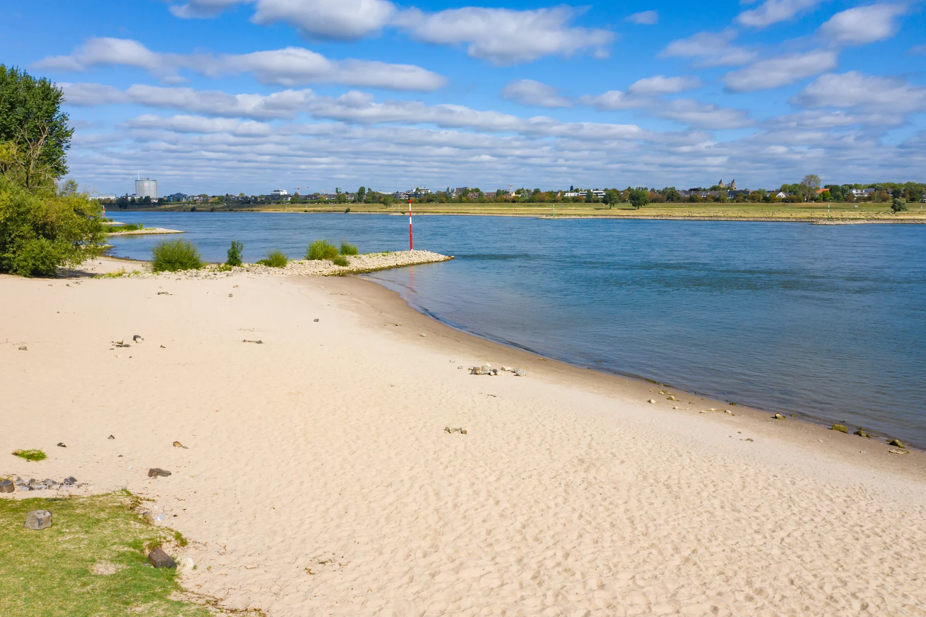 Mehrstöckige Wohnhäuser am Flussufer mit Fußgängern und Wasser im Vordergrund.