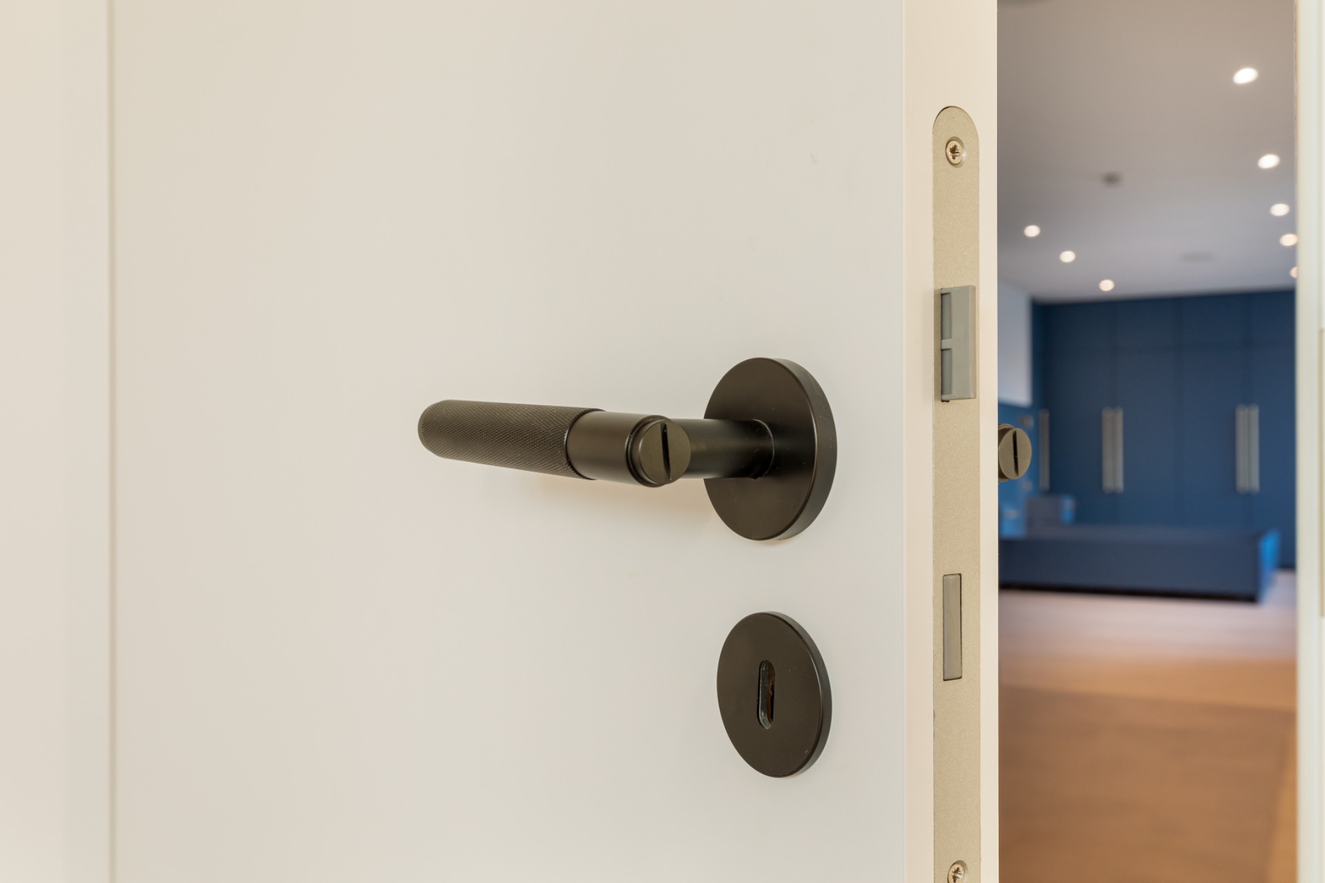 Geöffnete weiße Tür mit schwarzem Türgriff, dahinter ein Raum mit blauer Wand und Lichtern.