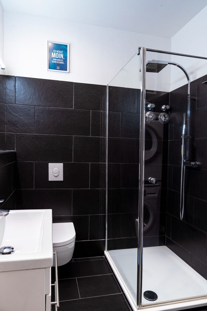Modernes Bad mit schwarzer Fliesenwand, Dusche, WC und Waschbecken.