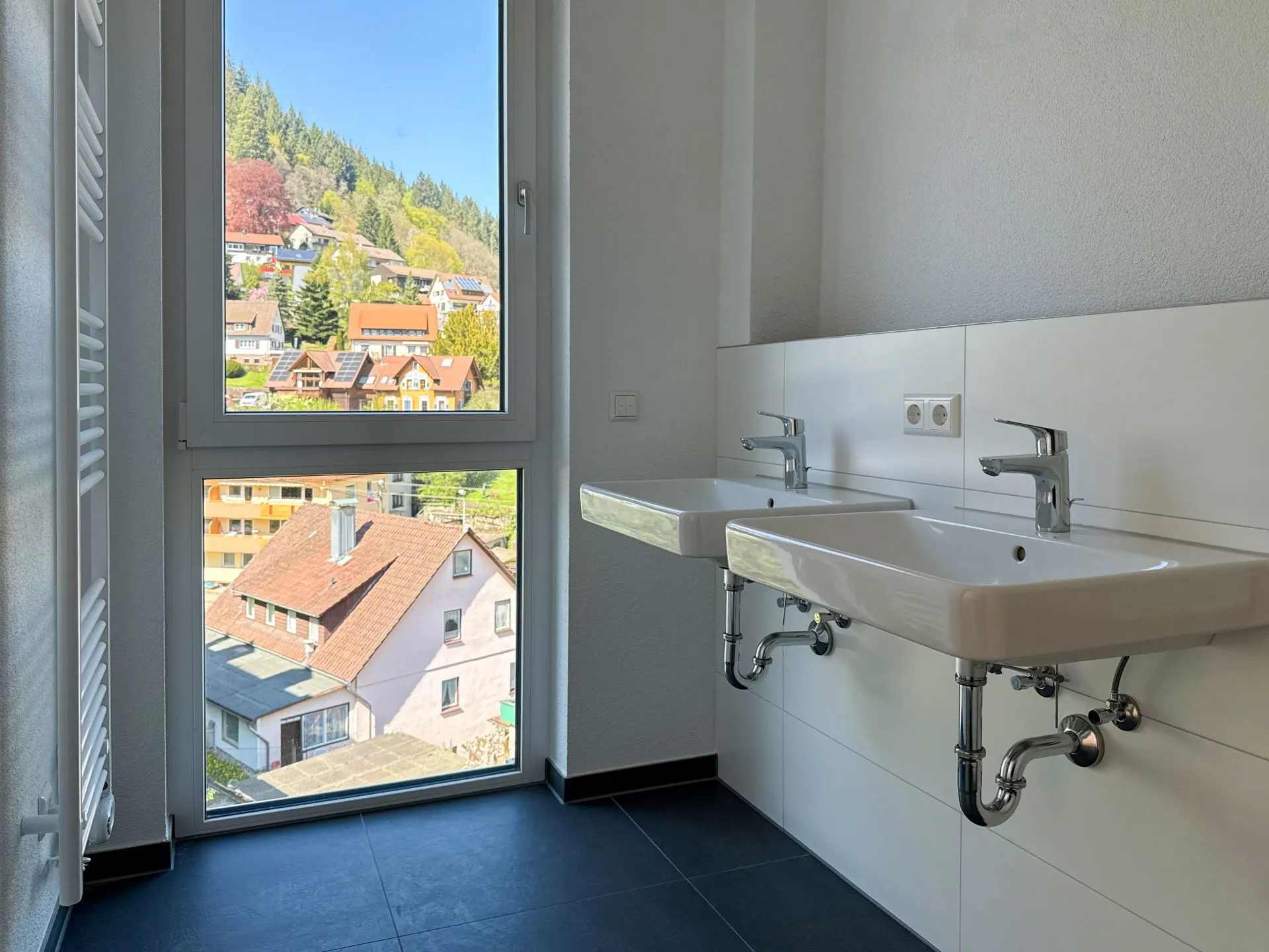 Zwei Waschbecken im modernen Bad mit großem Fenster und Blick auf Häuser und Bäume.