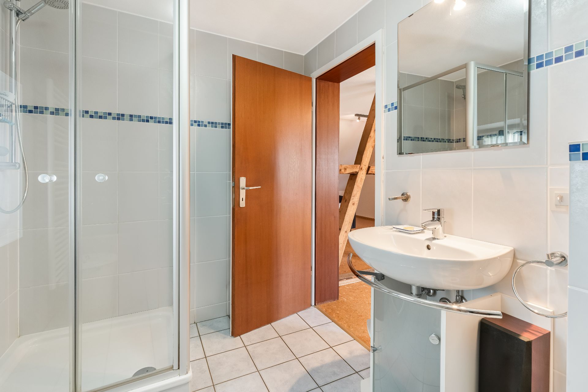 Modernes Badezimmer mit Dusche, Waschbecken, Spiegel und geöffneter Holztür.