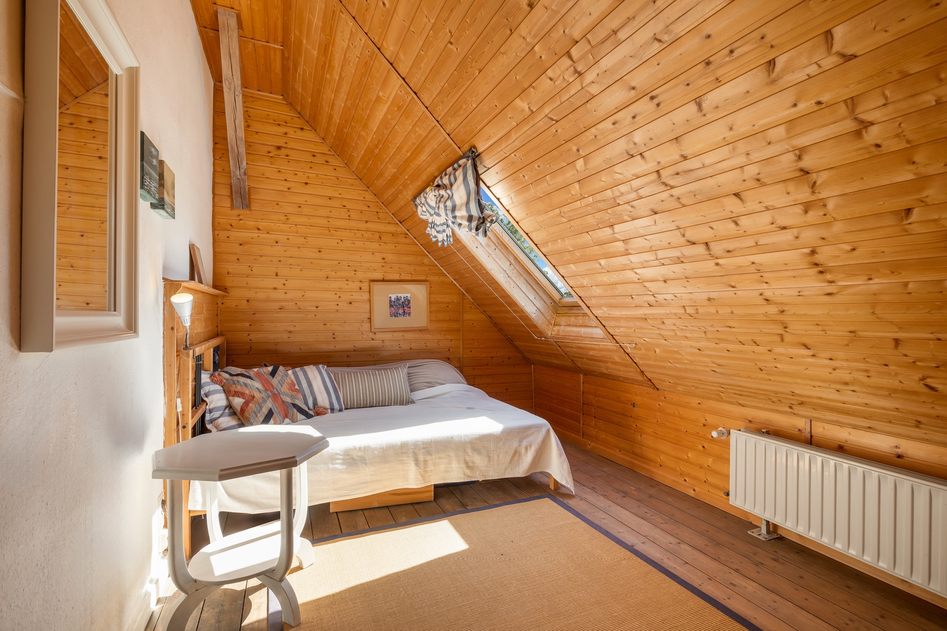 Helles Schlafzimmer mit Holzverkleidung, Bett, Fenster im Dach und kleiner Tisch.