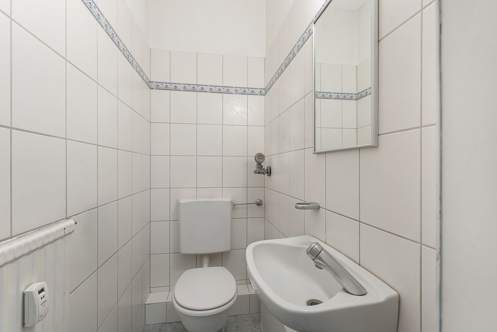 Kleines Badezimmer mit Toilette, Waschbecken und Spiegel, gefliest in Weiß.