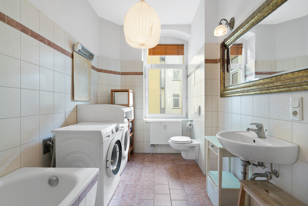 Helles Badezimmer mit Waschmaschine, Trockner, Badewanne, Waschbecken, Spiegel und WC.