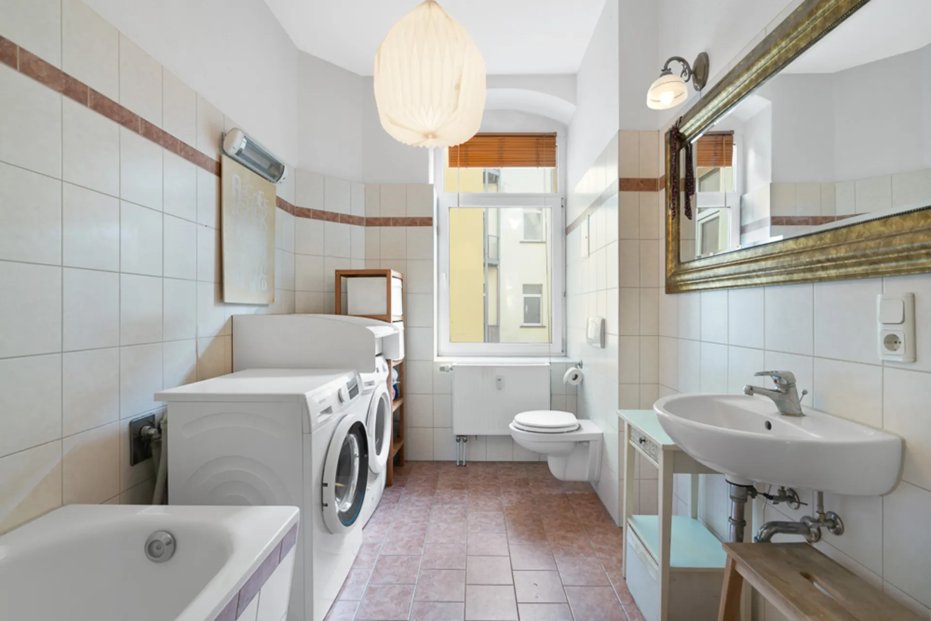 Helles Badezimmer mit Waschmaschine, Trockner, Badewanne, Waschbecken, Spiegel und WC.