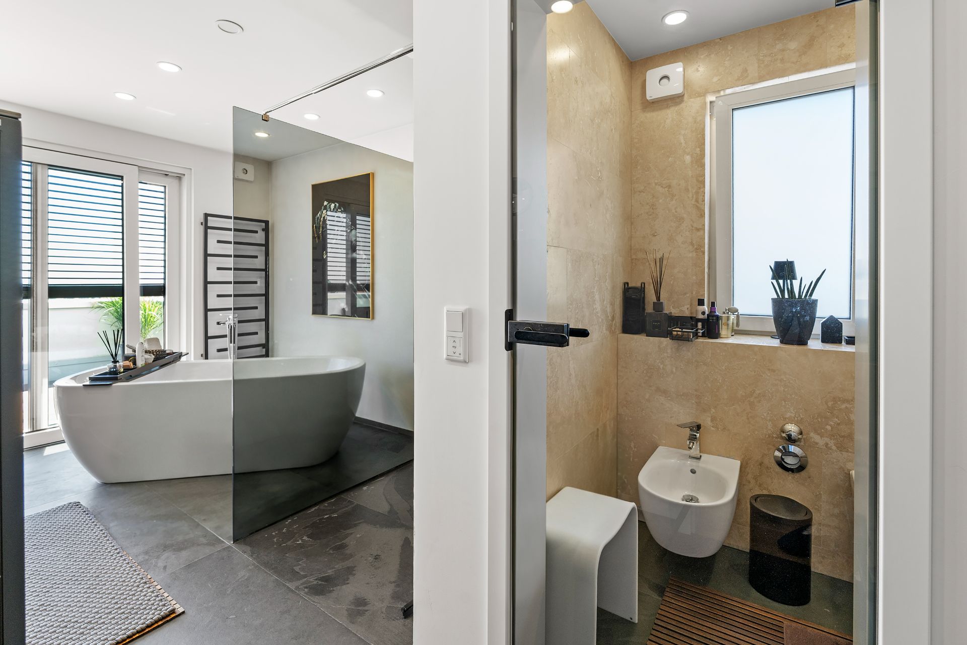 Modernes Badezimmer mit freistehender Badewanne, Bidet, WC und großem Fenster.