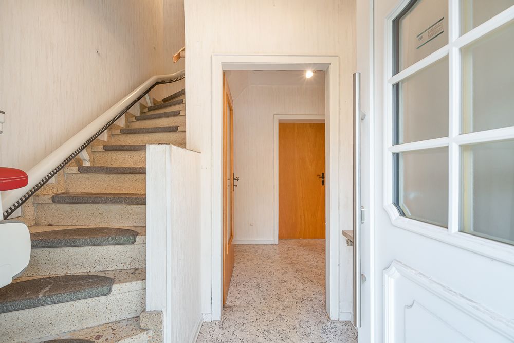 Eingangsbereich mit offener Tür, Treppe mit Treppenlift und Blick auf Flur und Holztür.
