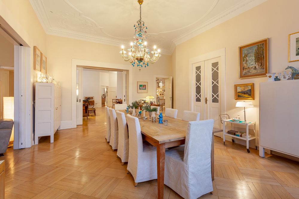 Helles Esszimmer mit großem Holztisch, acht Stühlen, Kronleuchter und Parkettboden.