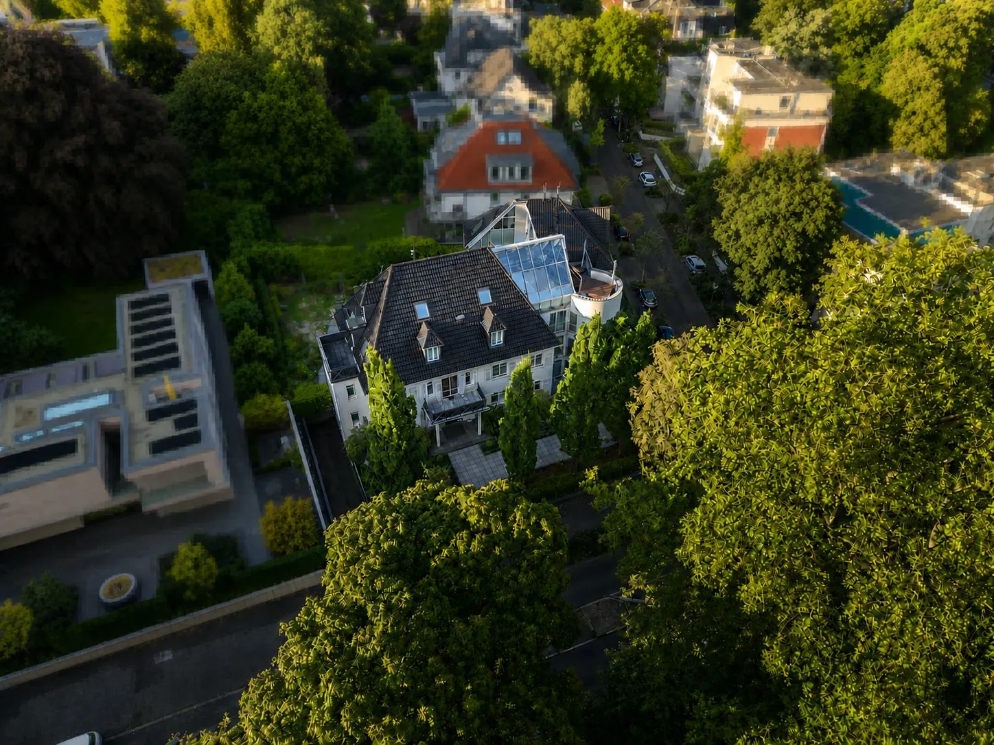 Luftaufnahme eines Wohnhauses mit Wintergarten, umgeben von Bäumen und Nachbarhäusern.
