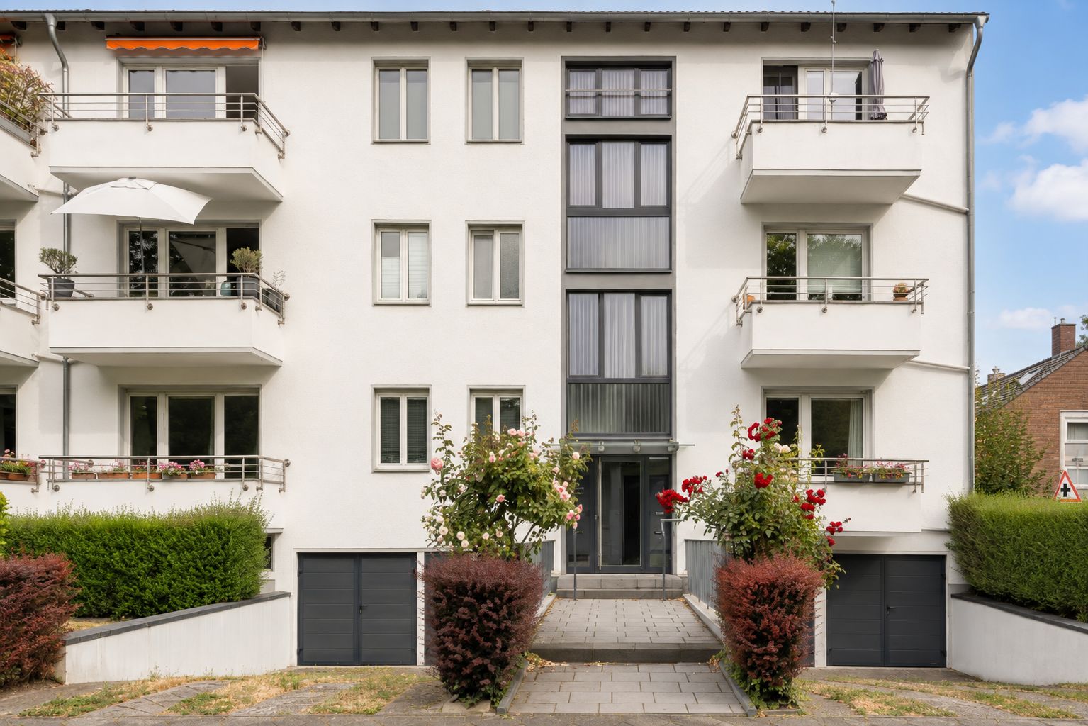 Mehrfamilienhaus mit Balkonen, Garagen und bepflanztem Eingangsbereich.