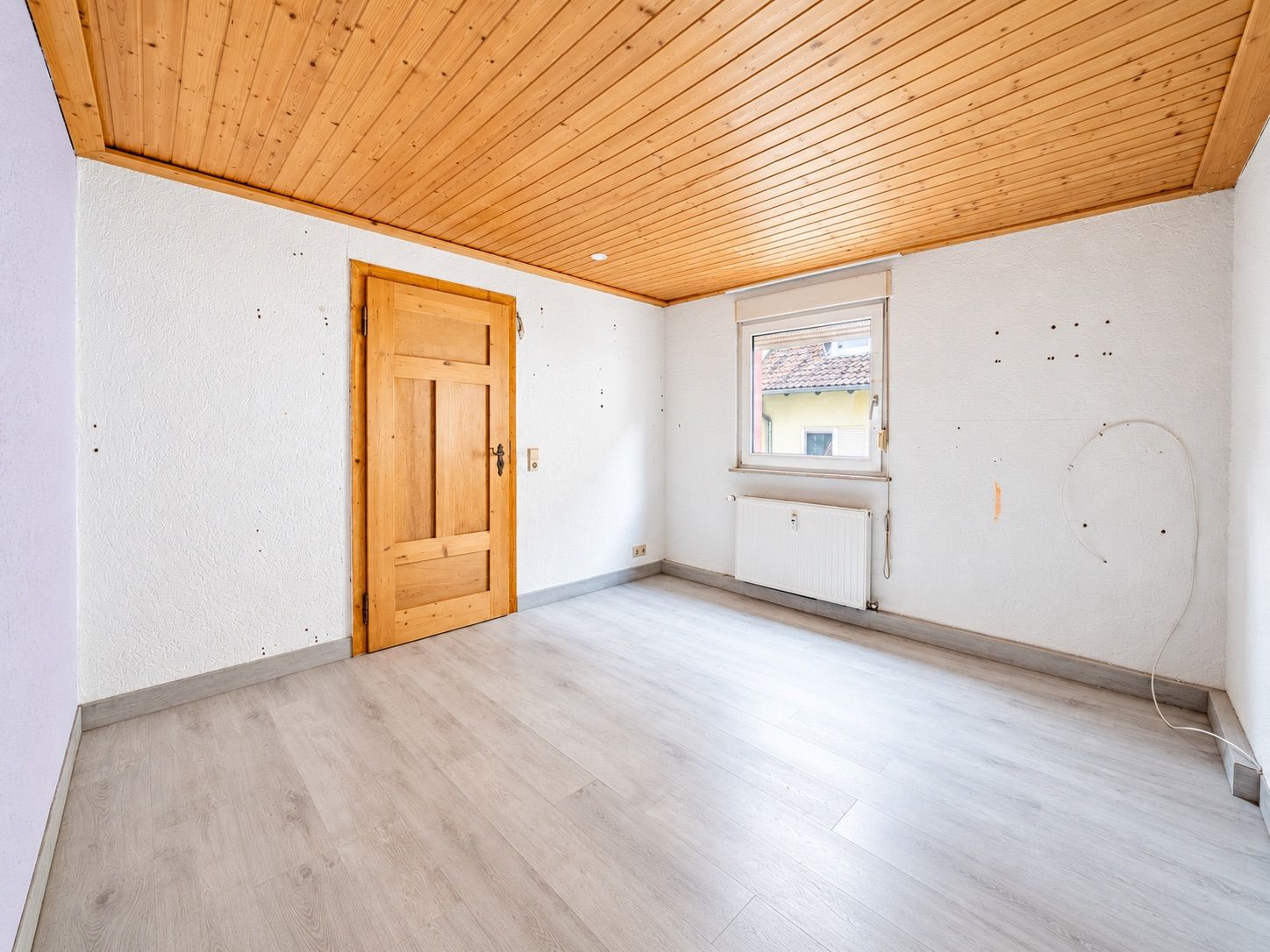 Leerer Raum mit Holztür, Holzdecke, Fenster und hellem Boden.