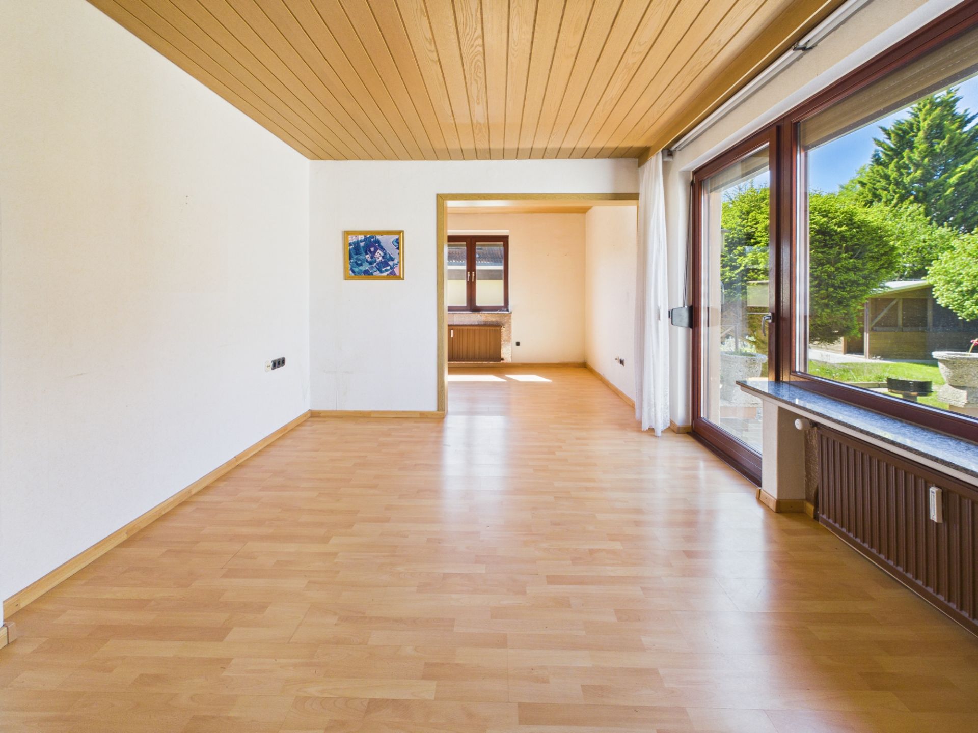 Helles Wohnzimmer mit Holzdecke, großem Fenster und Blick in den Garten.