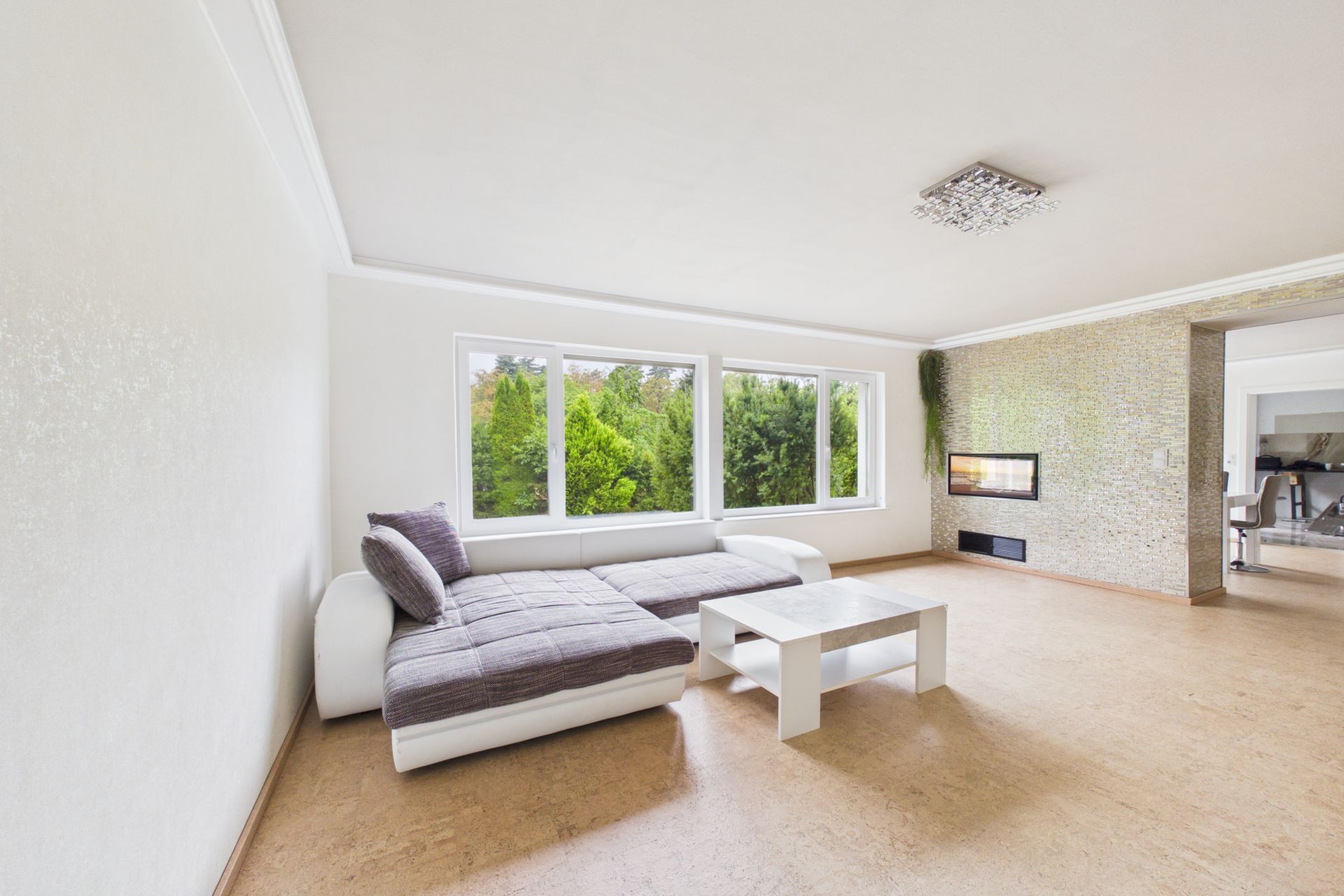 Helles Wohnzimmer mit Ecksofa, Couchtisch und großen Fenstern mit Blick ins Grüne.