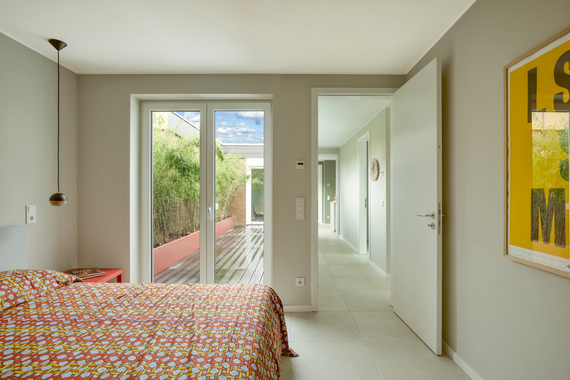 Helles Schlafzimmer mit Doppelbett, Glastür zur Terrasse und Blick auf einen Flur.