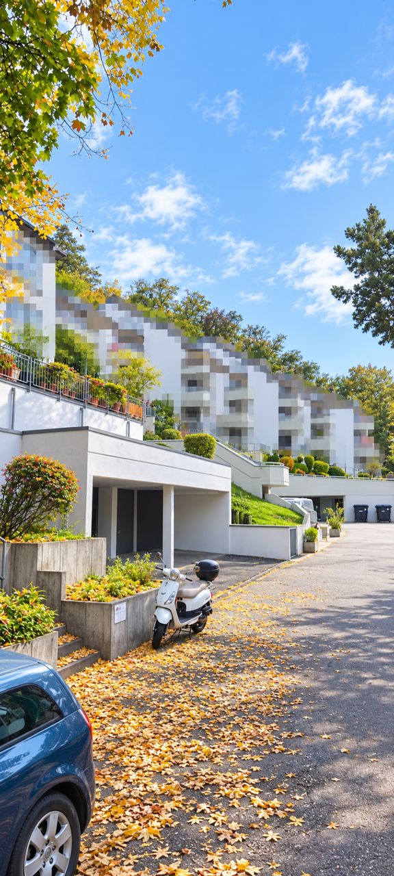 Mehrfamilienhaus mit Balkonen, Auto und Roller, Herbstlaub auf dem Boden.