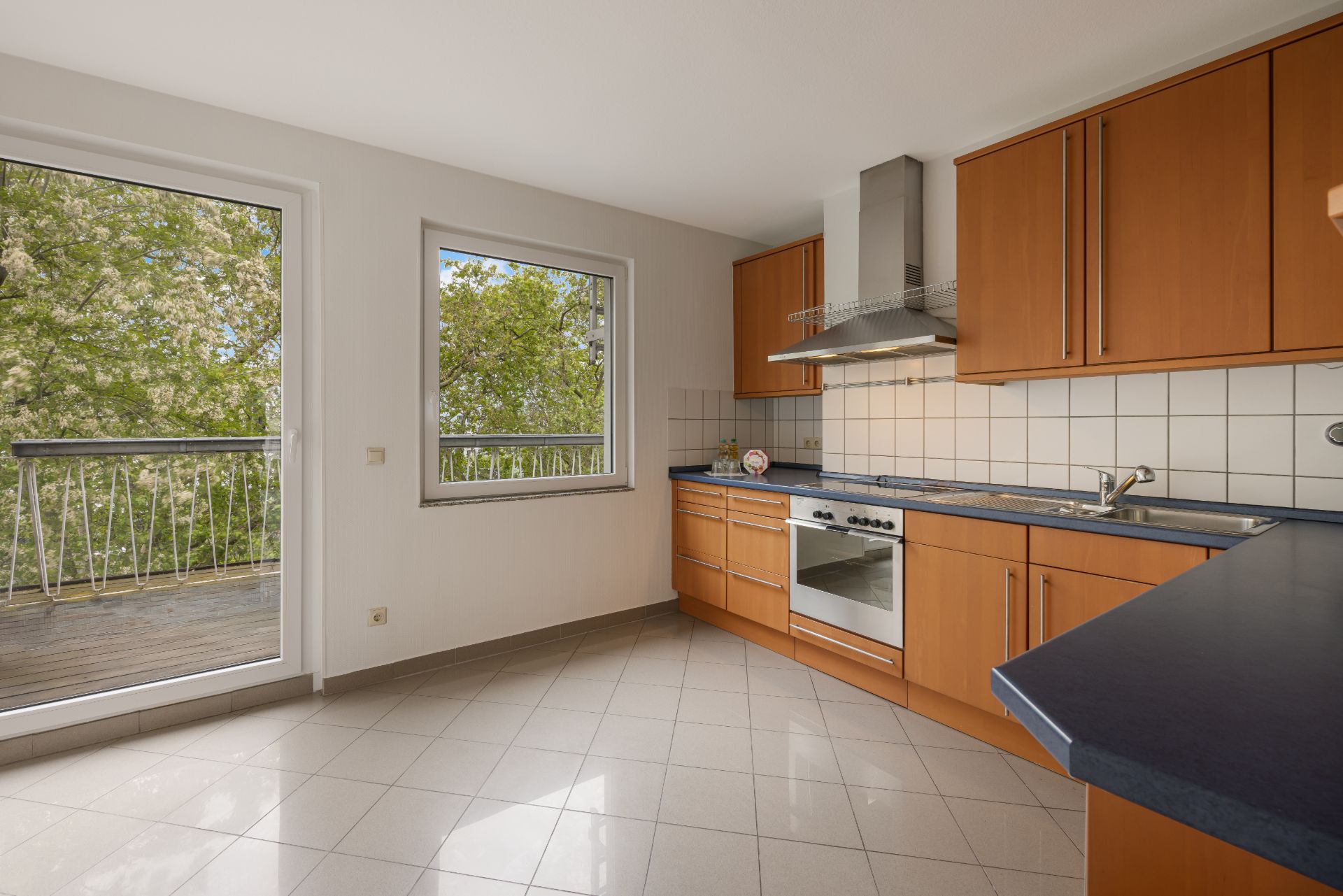 Helle Einbauküche mit Holzfronten, Fenster, Tür zum Balkon und Blick ins Grüne.