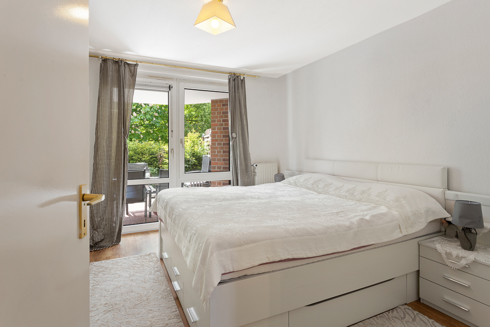 Helles Schlafzimmer mit Doppelbett, Nachttischen und Zugang zur Terrasse mit Gartenblick.