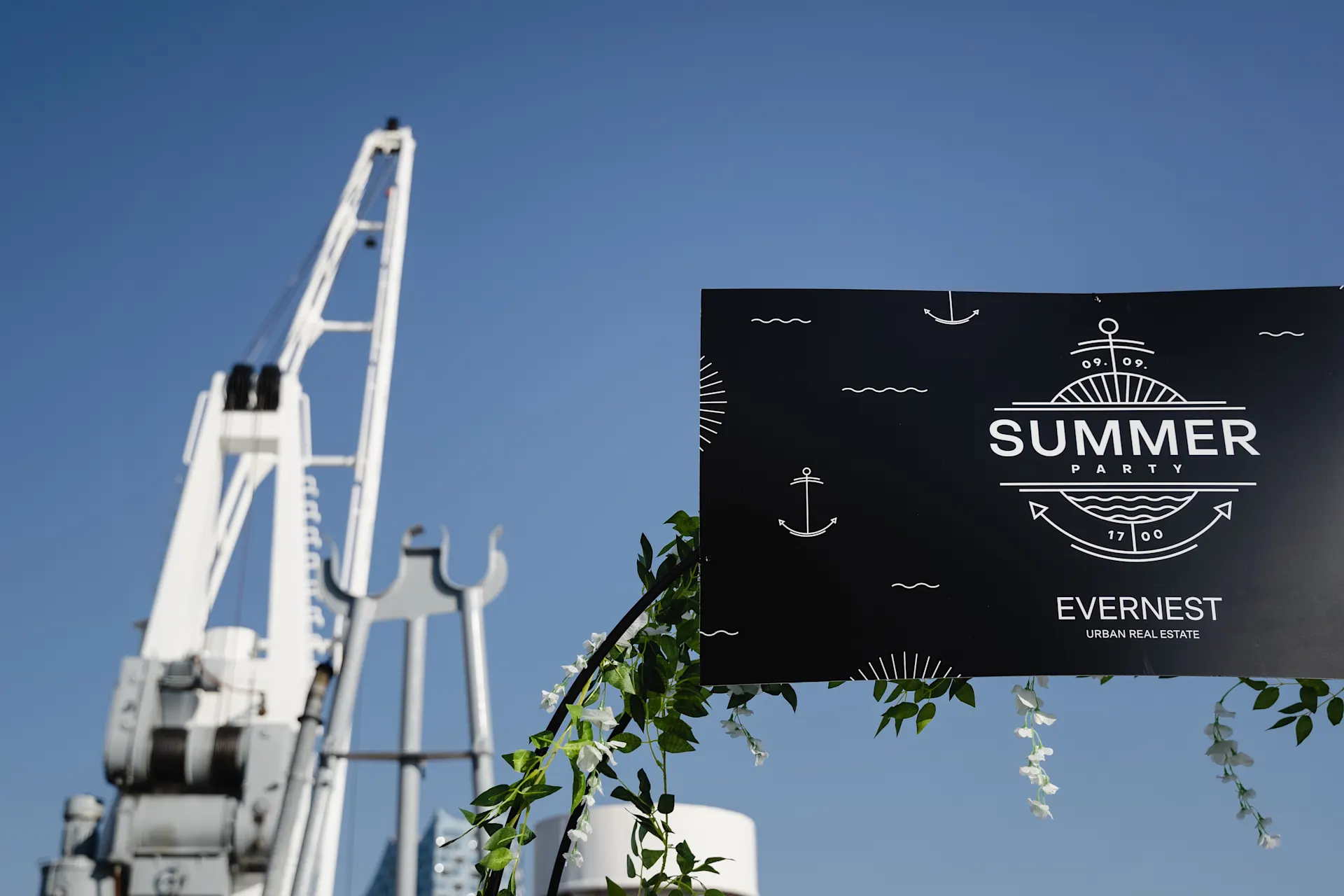Kran und dekoratives Schild mit Aufschrift 'Summer Party' vor blauem Himmel.