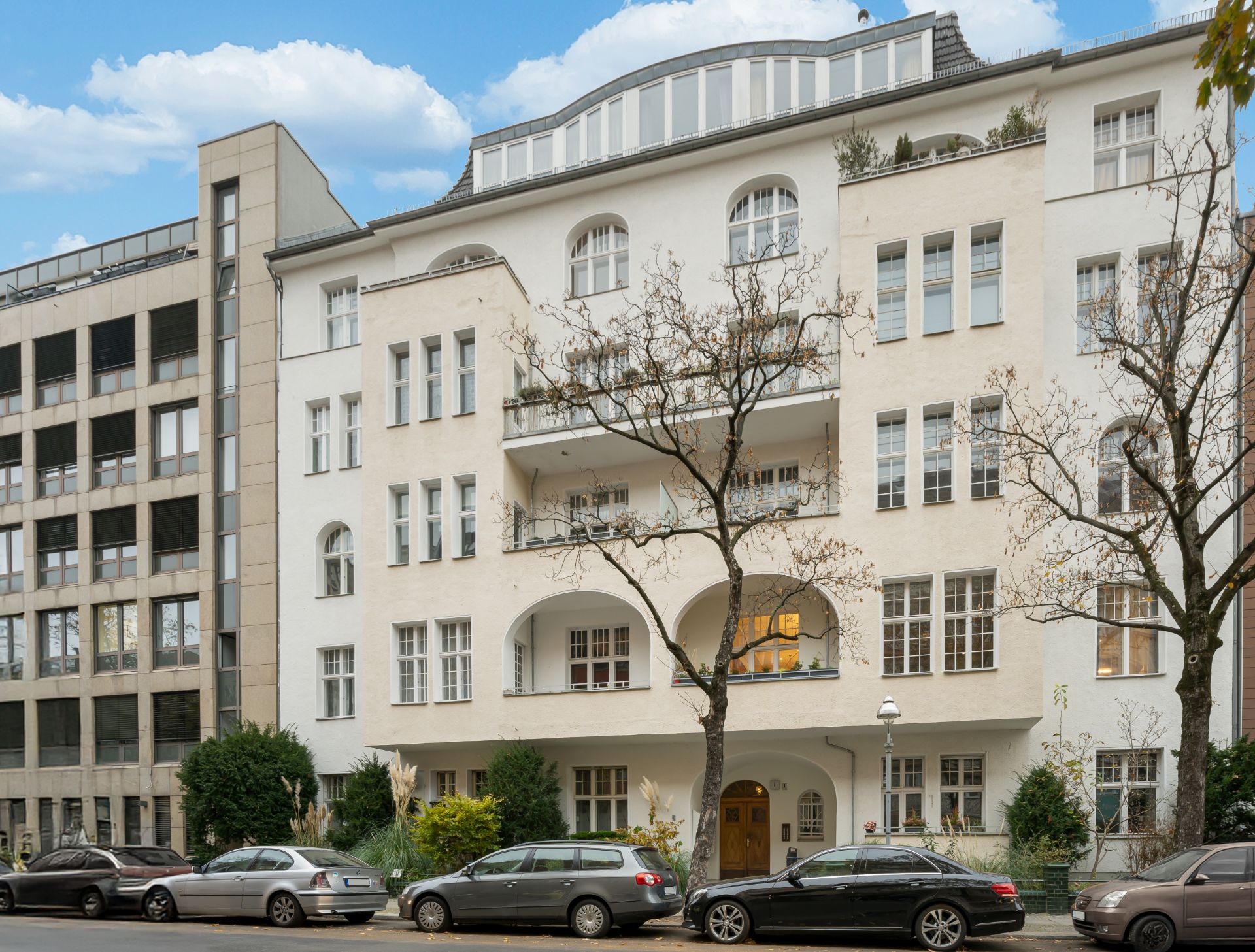 Mehrstöckiges Wohngebäude mit Balkonen und Autos, die am Straßenrand parken.