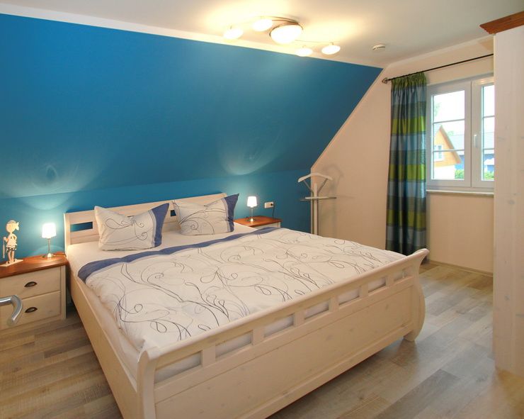Helles Schlafzimmer mit Doppelbett, blauer Wand, zwei Nachttischen und Fenster mit Vorhang.