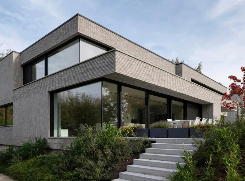 Modernes zweistöckiges Wohnhaus mit großen Fenstern und Garten, außen Treppe zum Eingang.