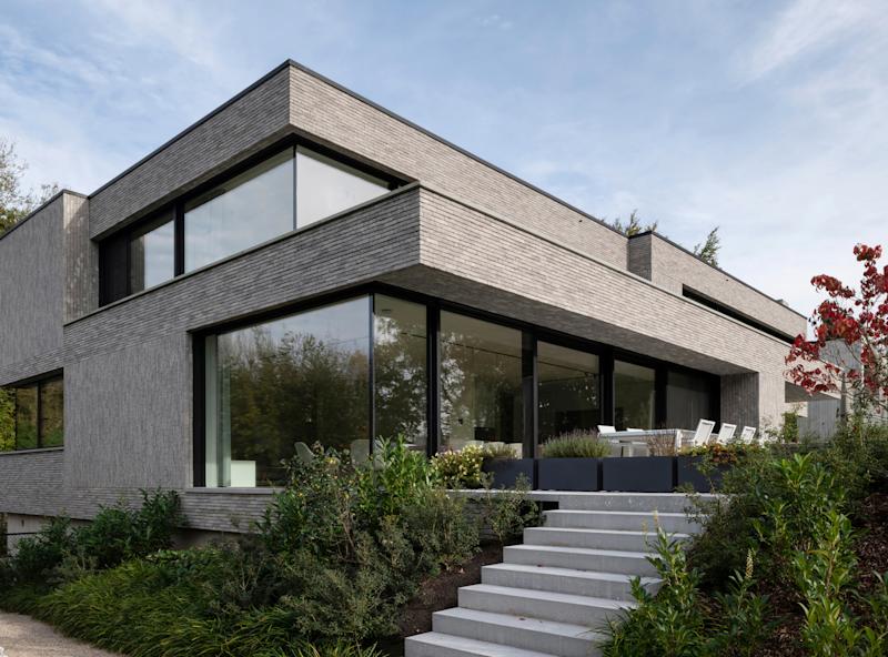 Modernes zweistöckiges Wohnhaus mit großen Fenstern und Garten, außen Treppe zum Eingang.