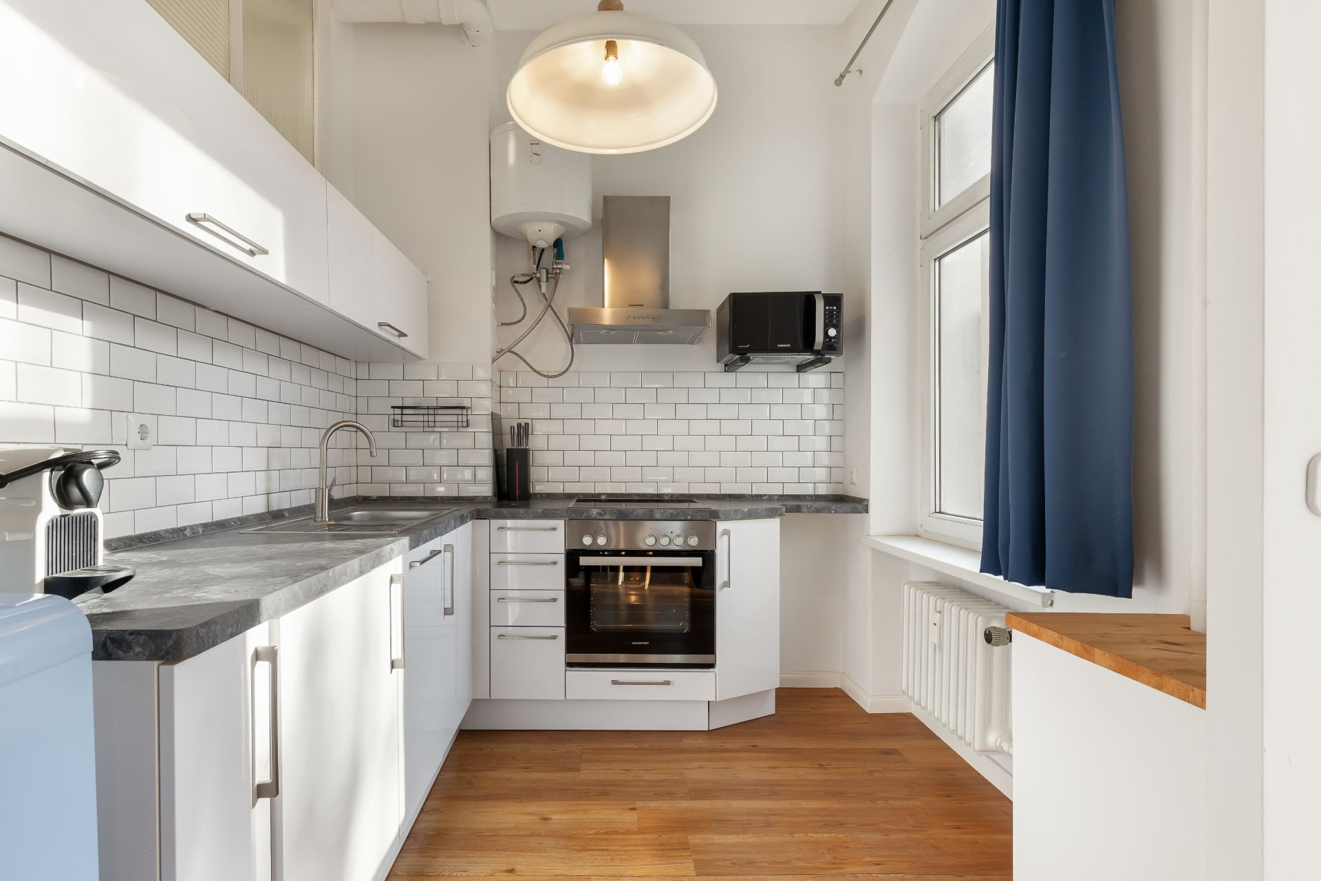 Moderne weiße Einbauküche mit Holzfußboden, Fenster und blauen Vorhängen.
