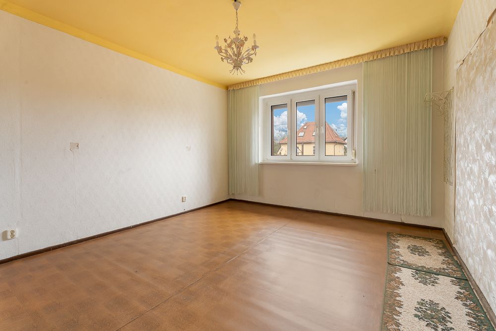Leerer Raum mit gelber Decke, Kronleuchter, Fenster und hellem Teppich am Rand.
