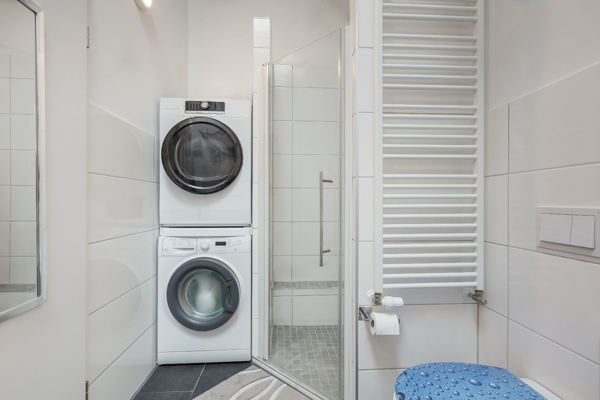 Modernes Badezimmer mit Waschmaschine, Trockner, Dusche, Handtuchheizung und Bügelbrett.