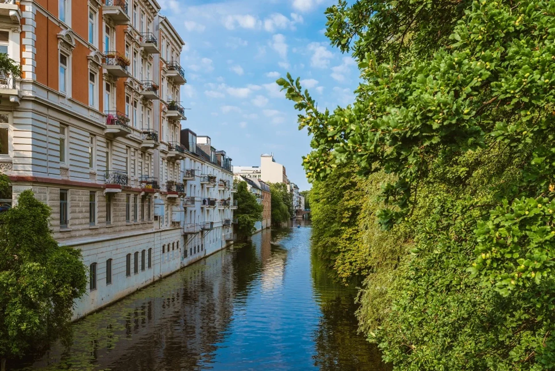 Mehrstöckiges Wohnhaus am Kanal mit Bäumen auf der rechten Seite.