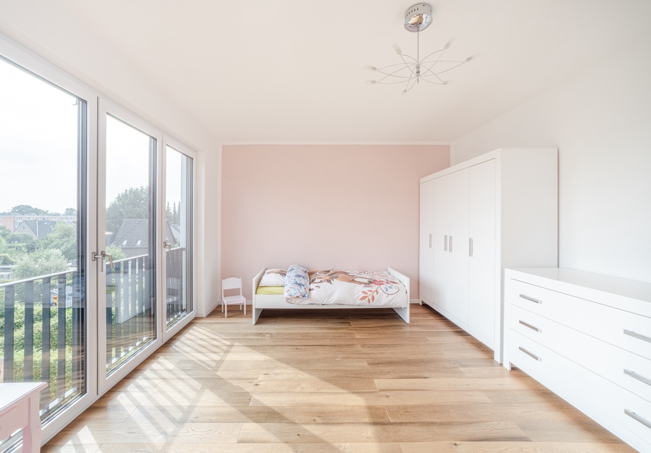 Helles Schlafzimmer mit Einzelbett, großem Fenster, weißem Kleiderschrank und Kommode.