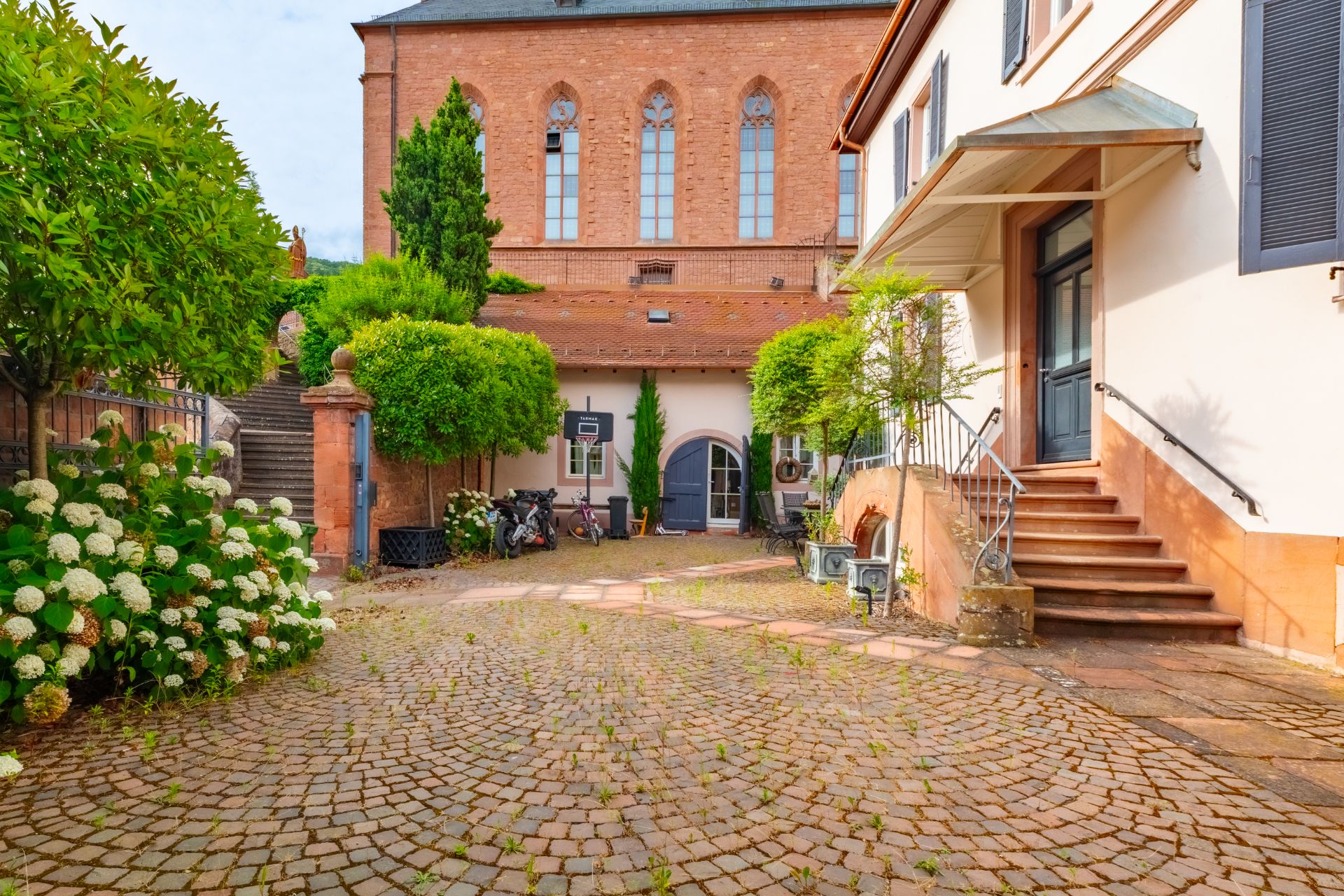Gepflasterter Innenhof mit Treppe, Pflanzen und Blick auf ein großes Backsteingebäude.