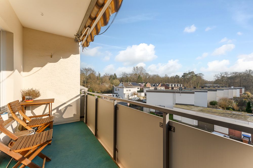 Balkon mit zwei Holzstühlen und Tisch, Blick auf Wohnhäuser und Bäume.