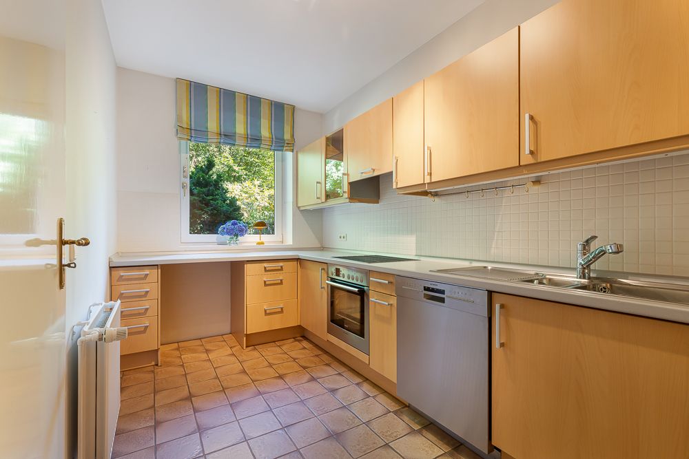 Moderne Küche mit Holzfronten, Fenster mit Rollos, Herd, Spülmaschine und Spüle.