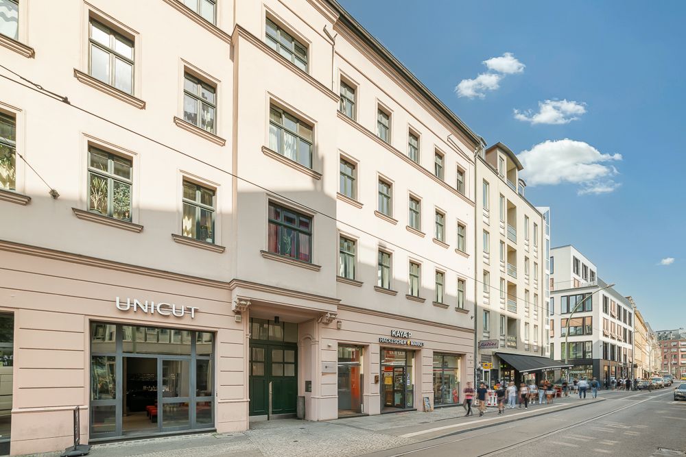 Mehrstöckiges Wohnhaus mit Geschäften im Erdgeschoss an einer belebten Straße bei Tag.