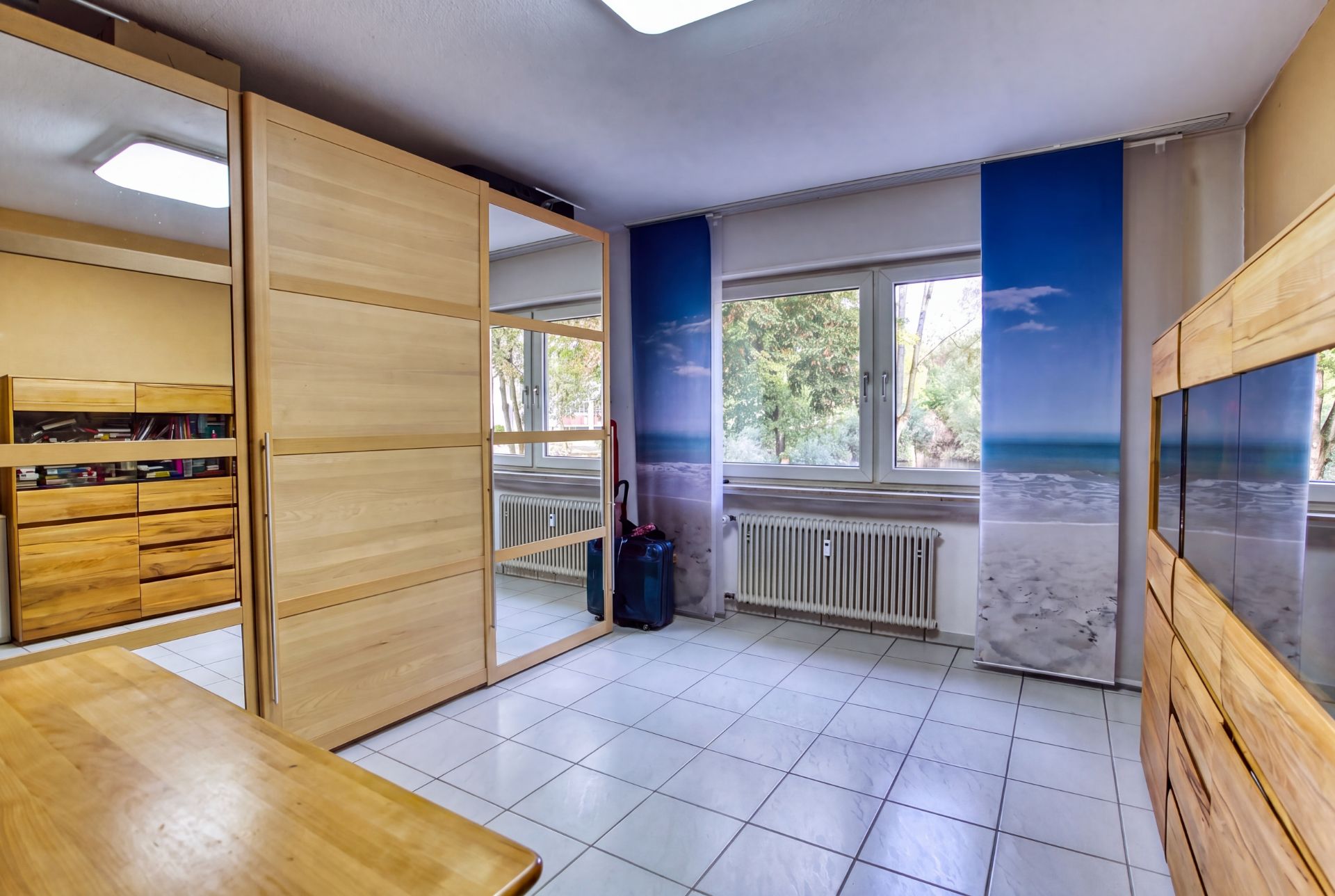 Helles Zimmer mit weißen Fliesen, Holzschränken und großem Fenster mit Meerblick-Fotovorhängen.