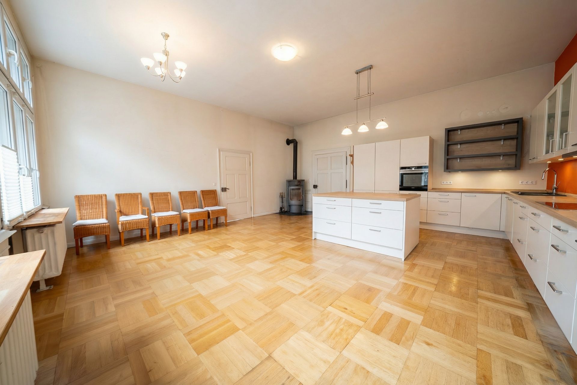 Große Wohnküche mit Holzfußboden, Kücheninsel und sieben Stühlen an der Wand.