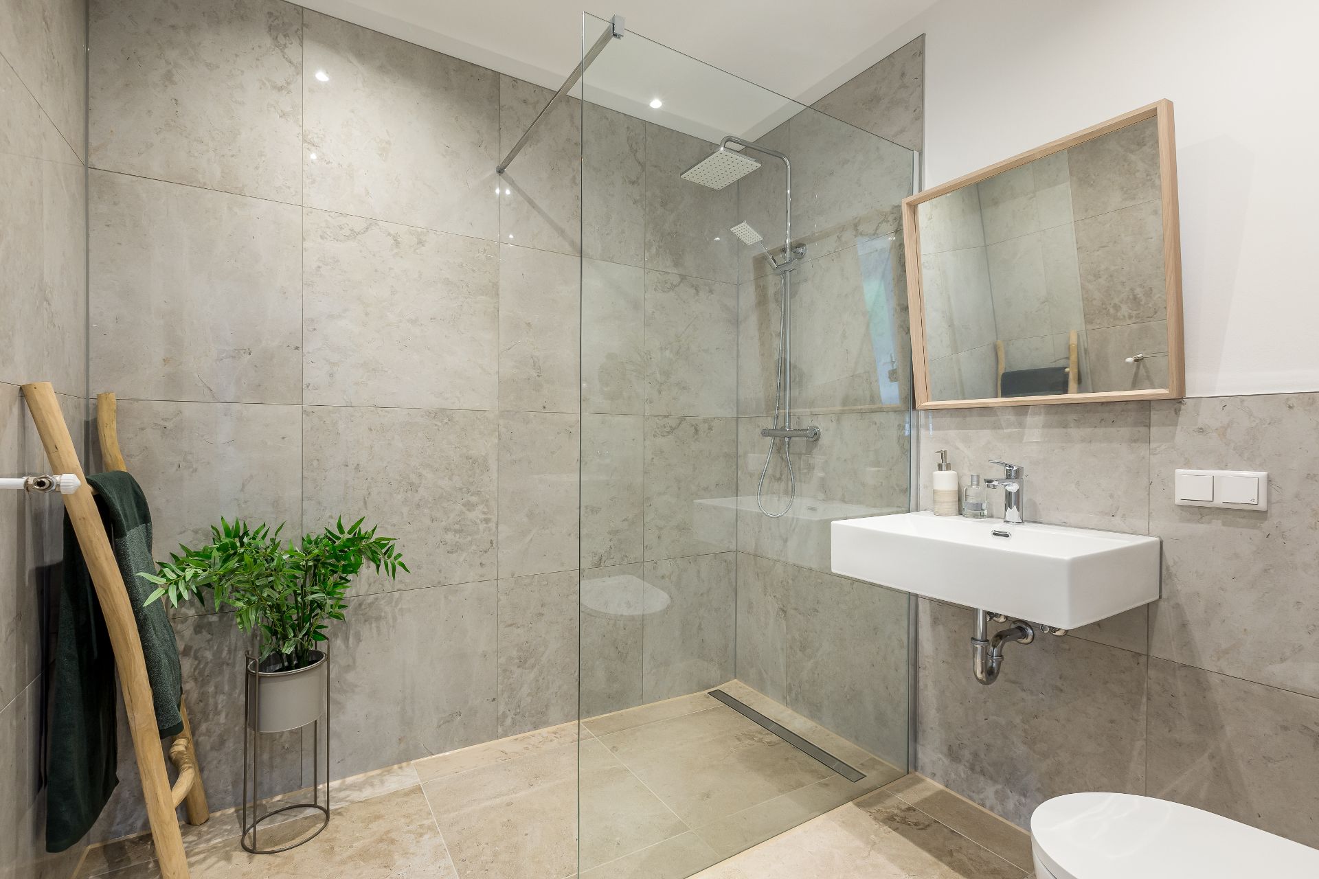 Modernes Badezimmer mit großer, ebenerdiger Dusche, Waschtisch, Spiegel und grüner Pflanze.