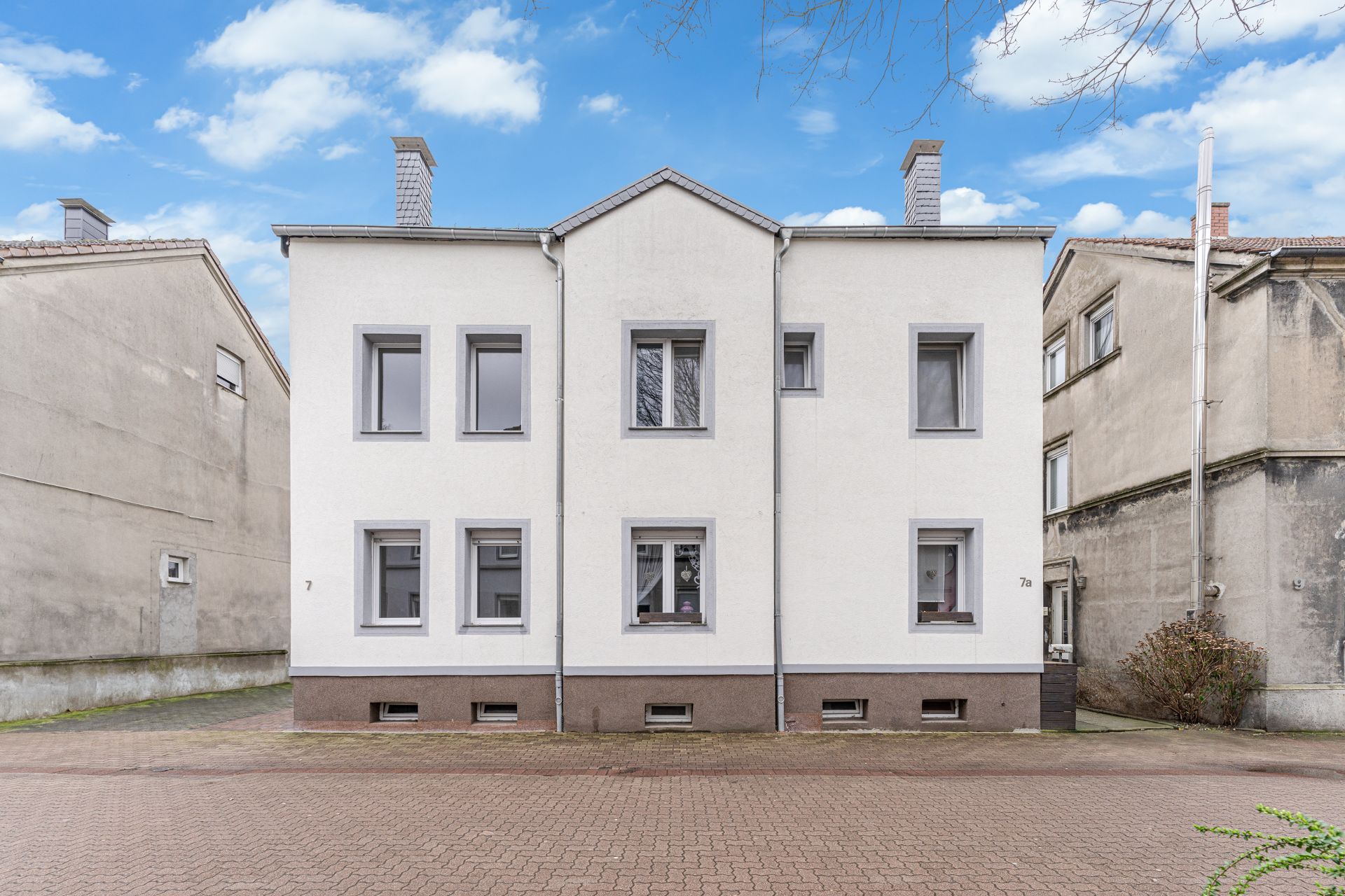 Vorderansicht eines zweistöckigen Wohnhauses mit weißer Fassade und mehreren Fenstern.