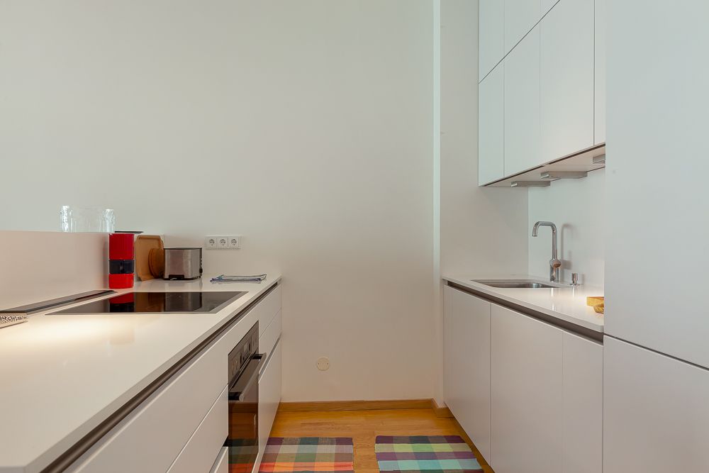 Moderne Küche mit weißen Schränken, Elektroherd, Spüle und buntem Teppich auf Holzboden.