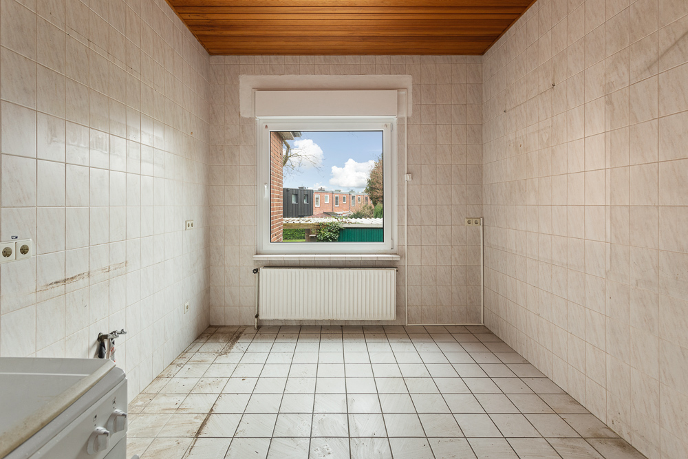 Leerer, gefliester Raum mit großem Fenster und Heizkörper, Holzbalkendecke.