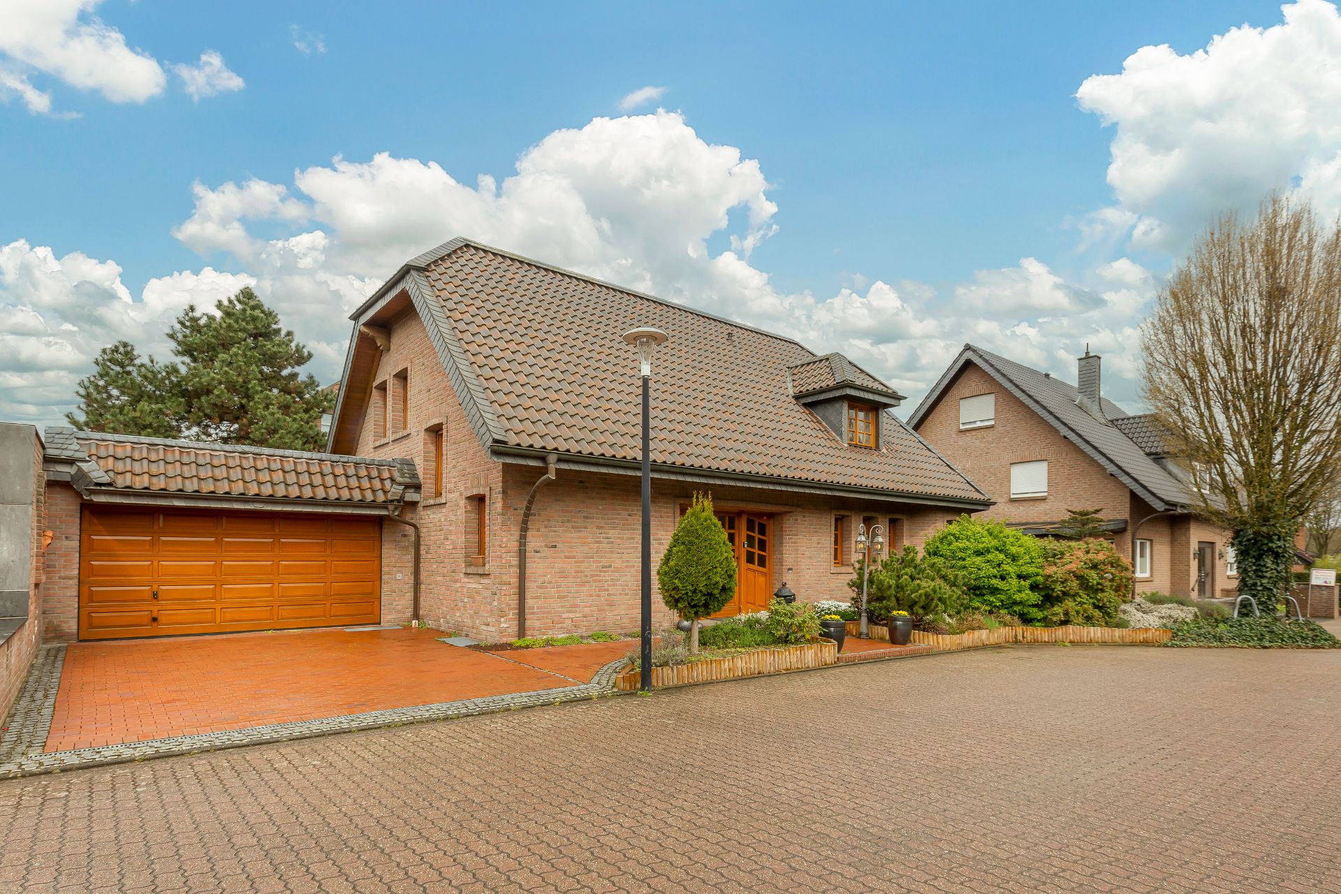 Backsteinwohnhaus mit Satteldach, Garage und bepflanztem Vorgarten bei Tageslicht.