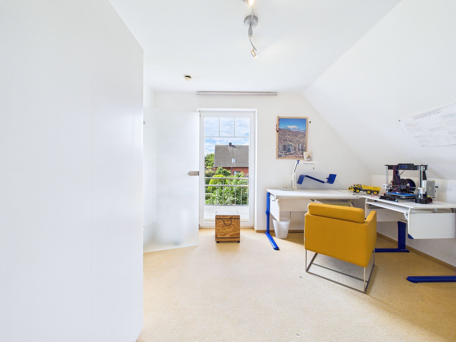 Helles Arbeitszimmer mit gelbem Stuhl, Schreibtisch, Fenster und Blick auf Häuser.